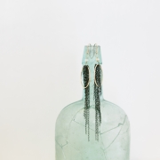 A pair of gold earrings with black chain dangling from the ear wire displayed on a blue green vintage bottle