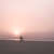 Fine art photograph by Paula McIntosh of PJM Photography showing a lone cyclist riding along the beach at sunrise under a soft pink sky and calm ocean horizon.